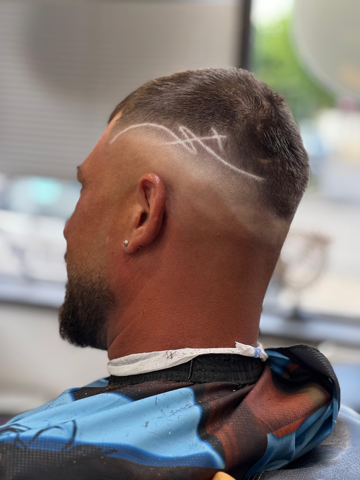 Skin fade înalt cu linie de design gravată pe lateral și barbă conturată